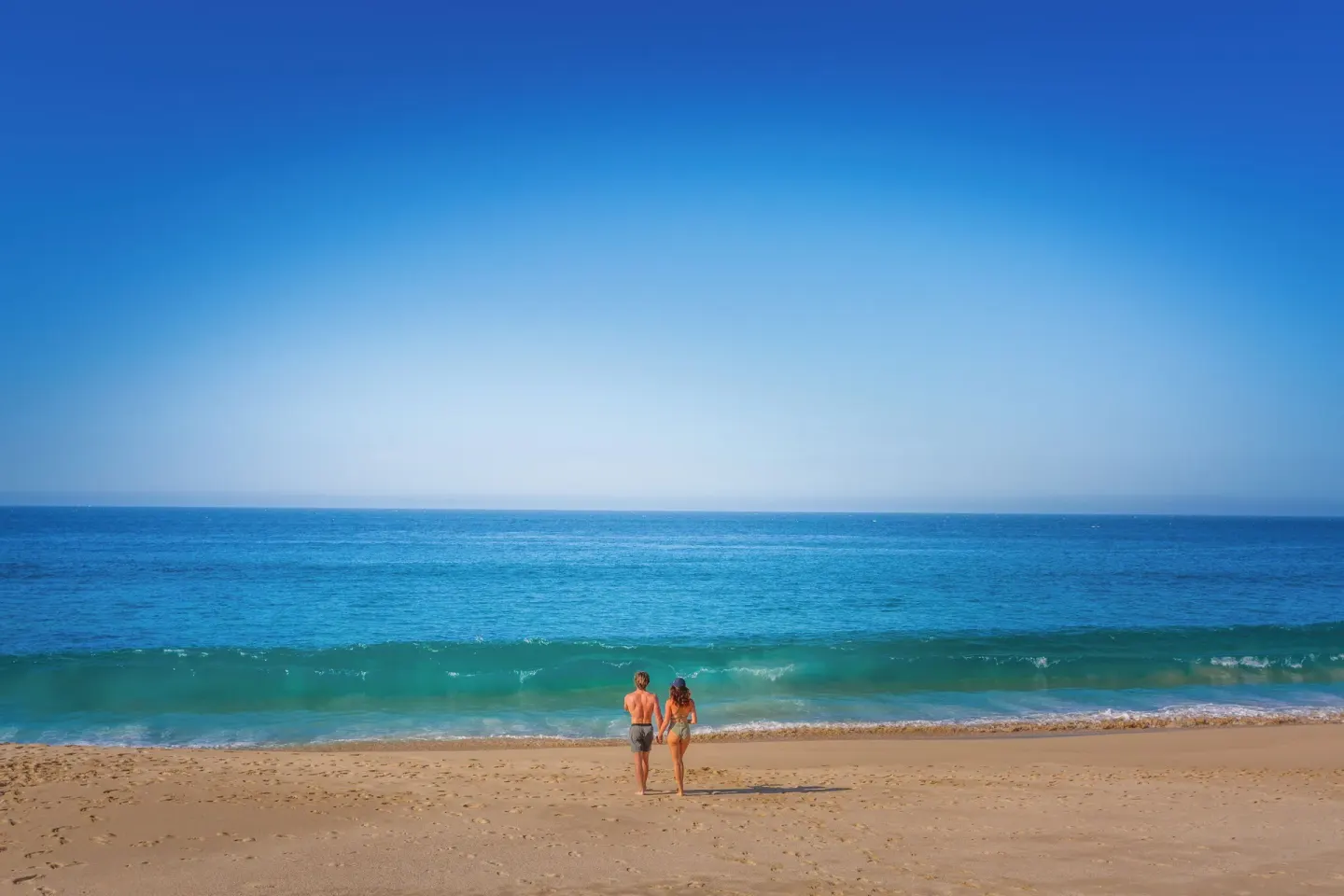 A couple stands at the shoreline with blue ocean ahead at Sandos Finisterra.