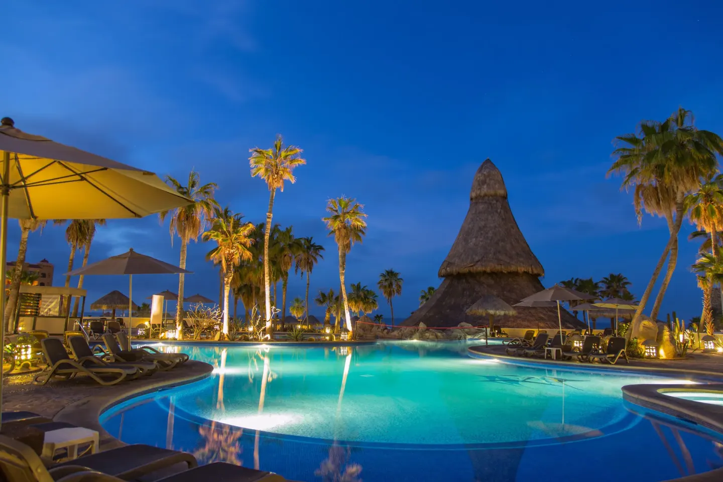 Illuminated pool with palms and a thatched-roof structure at Sandos Finisterra.