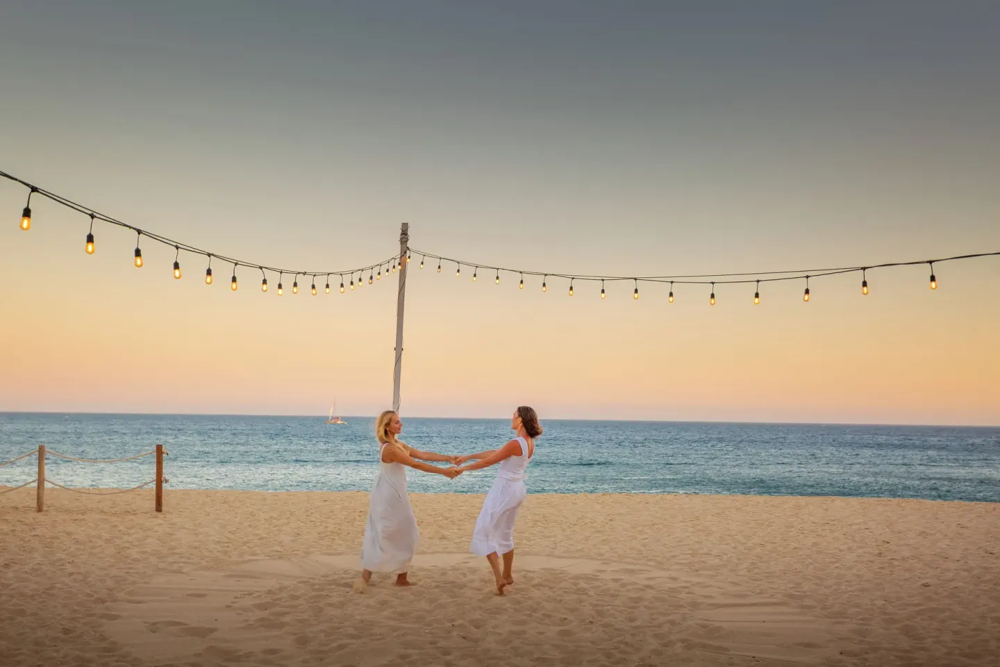 Two guests in white dresses dance on the beach at sunset at Sandos Finisterra.