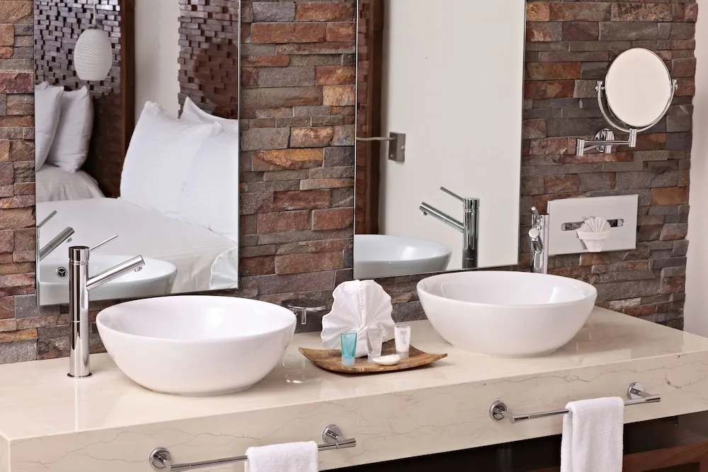 Junior Suite bathroom with twin vessel sinks, mirrors, stone wall, and towels at Sandos Finisterra.