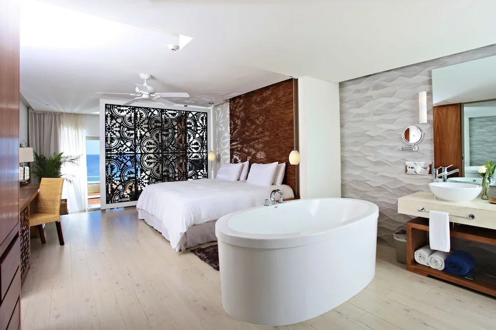 Junior Suite with king bed, soaking tub, vanity, and decorative screen at Sandos Finisterra.