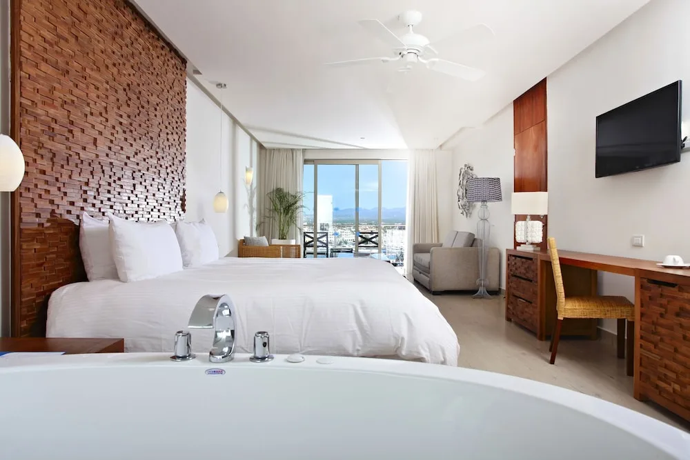 Junior Suite with king bed, tub edge, desk, armchair, and balcony view at Sandos Finisterra.