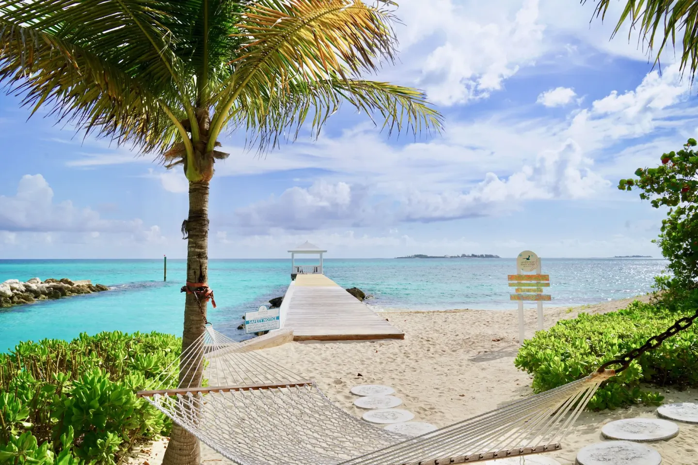 Beach hammock beside a white pier and turquoise water at Sandyport Beach Resort.