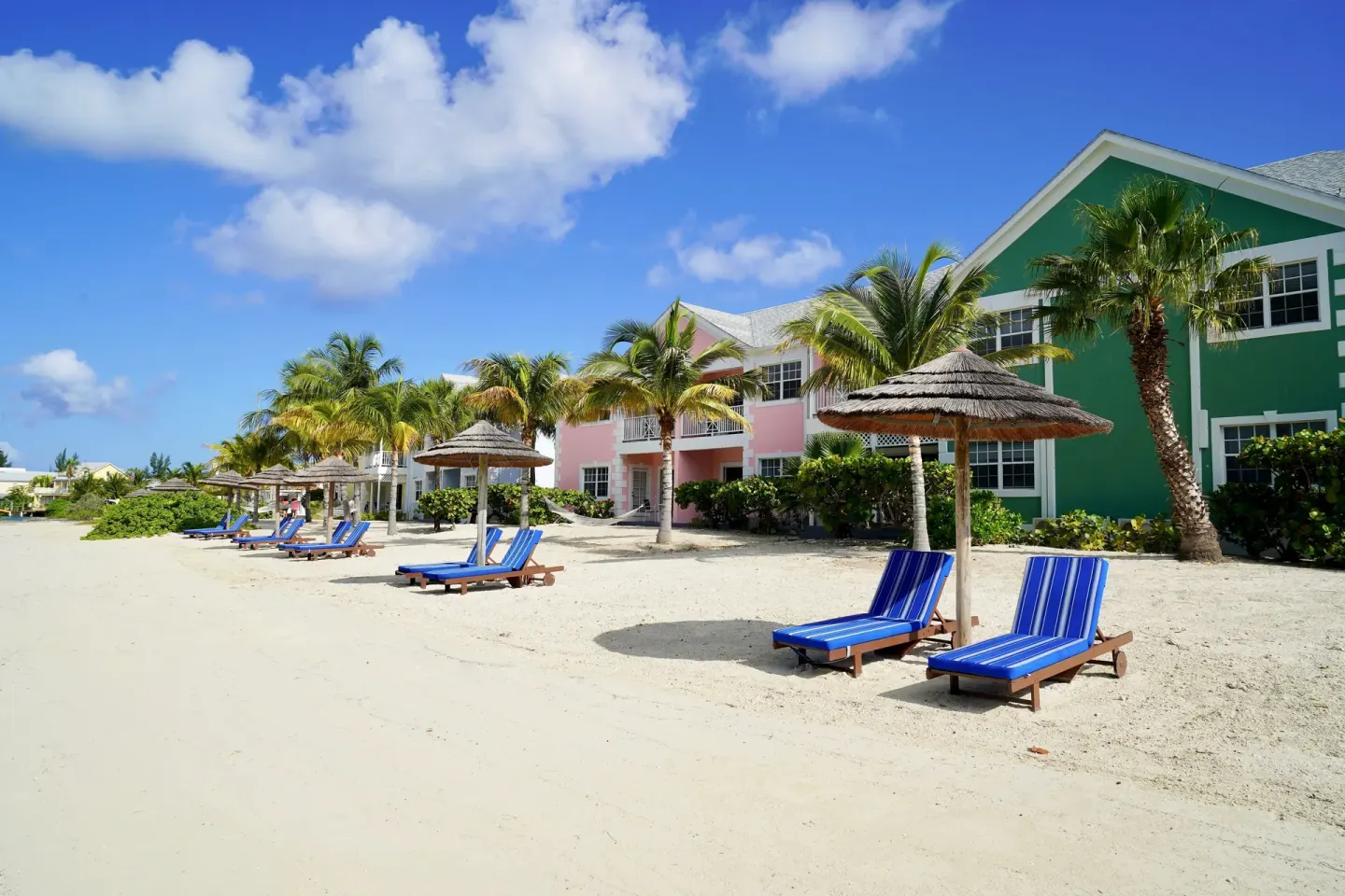 Beach loungers and thatched shades outside colorful buildings at Sandyport Beach Resort.