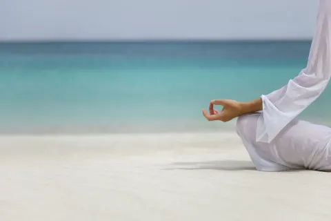 A person meditates on the white sand beside turquoise water at Sandyport Beach Resort.