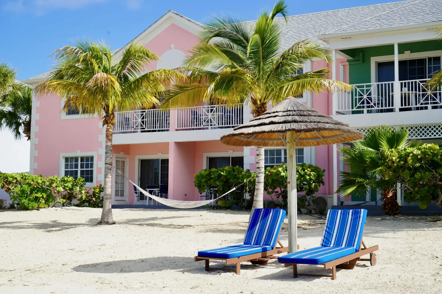Beachfront pastel building, palms, loungers and a hammock at Sandyport Beach Resort.