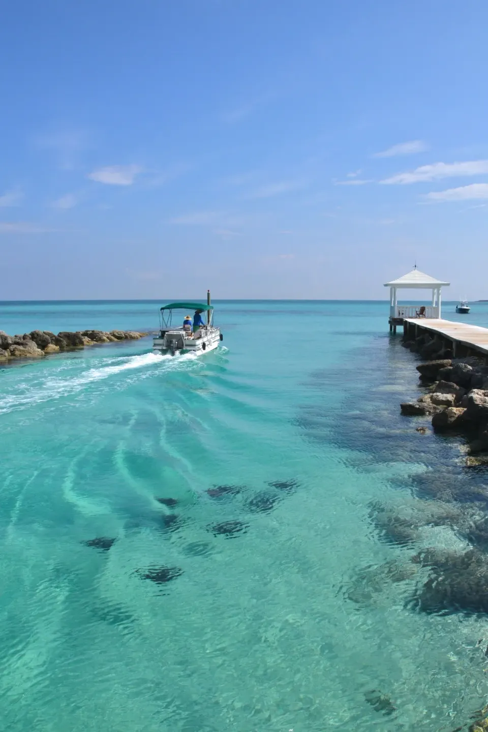 A small boat moves through clear turquoise water by Sandyport Beach Resort.