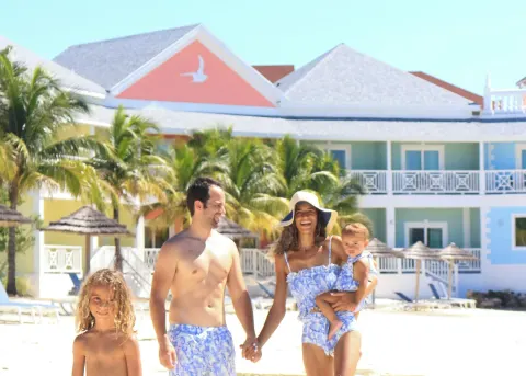 A family walks on the beach in front of colorful buildings at Sandyport Beach Resort.