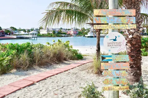 Colorful Sandyport Beach Resort sign beside a sandy lagoon path.