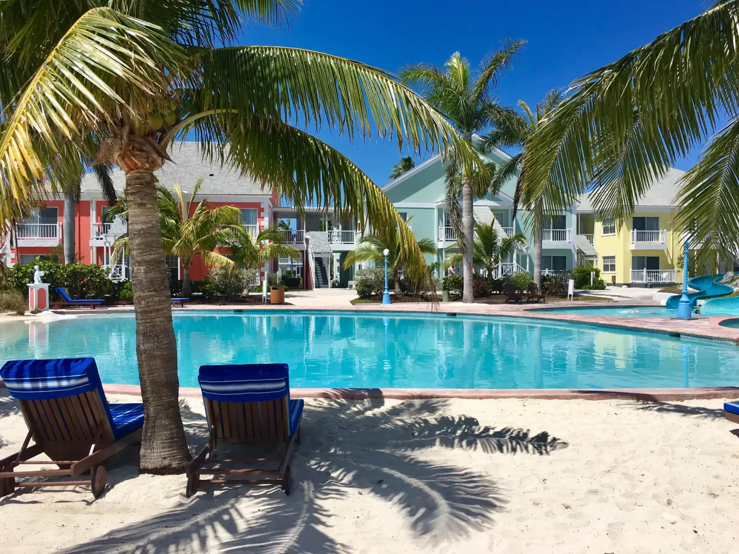 Palm-shaded loungers face the pool and pastel buildings at Sandyport Beach Resort.