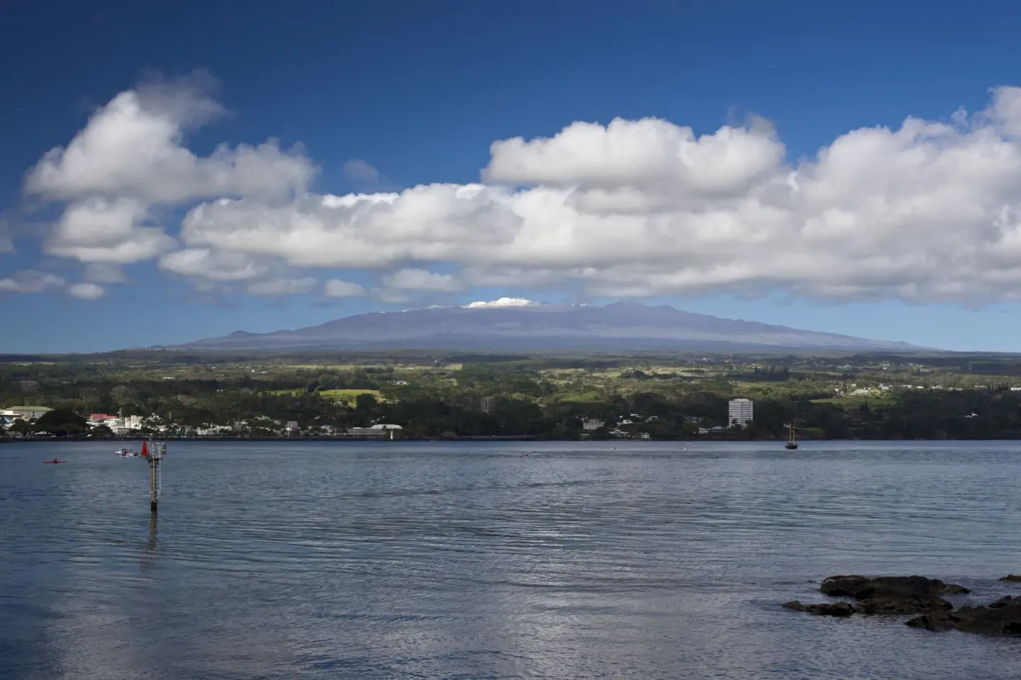 A wide bay view with shoreline, clouds, and distant mountain near SCP Hilo Hotel.