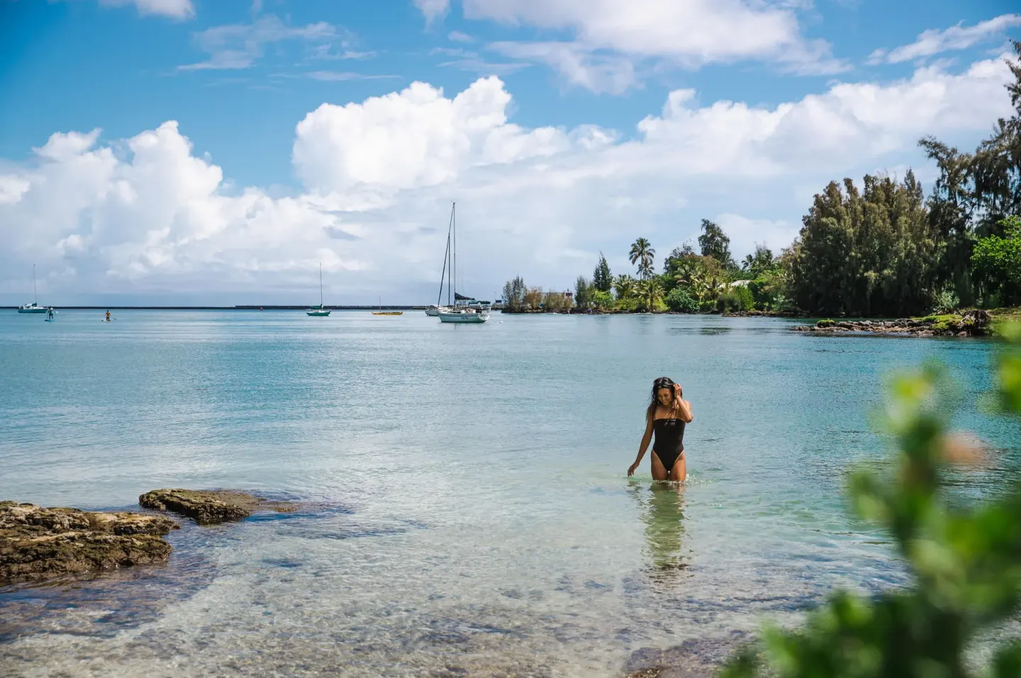 A swimmer wades in clear bay water near boats by SCP Hilo Hotel.