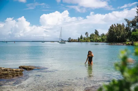 A swimmer wades in clear bay water near boats by SCP Hilo Hotel.