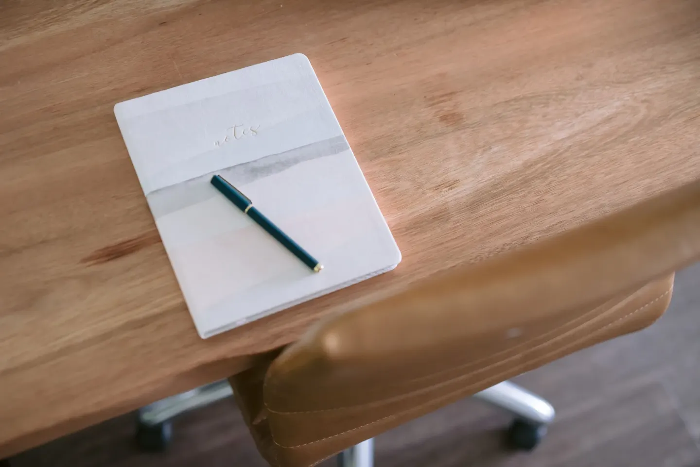 Notebook and pen on a wooden desk beside a chair at SCP Hilo Hotel.