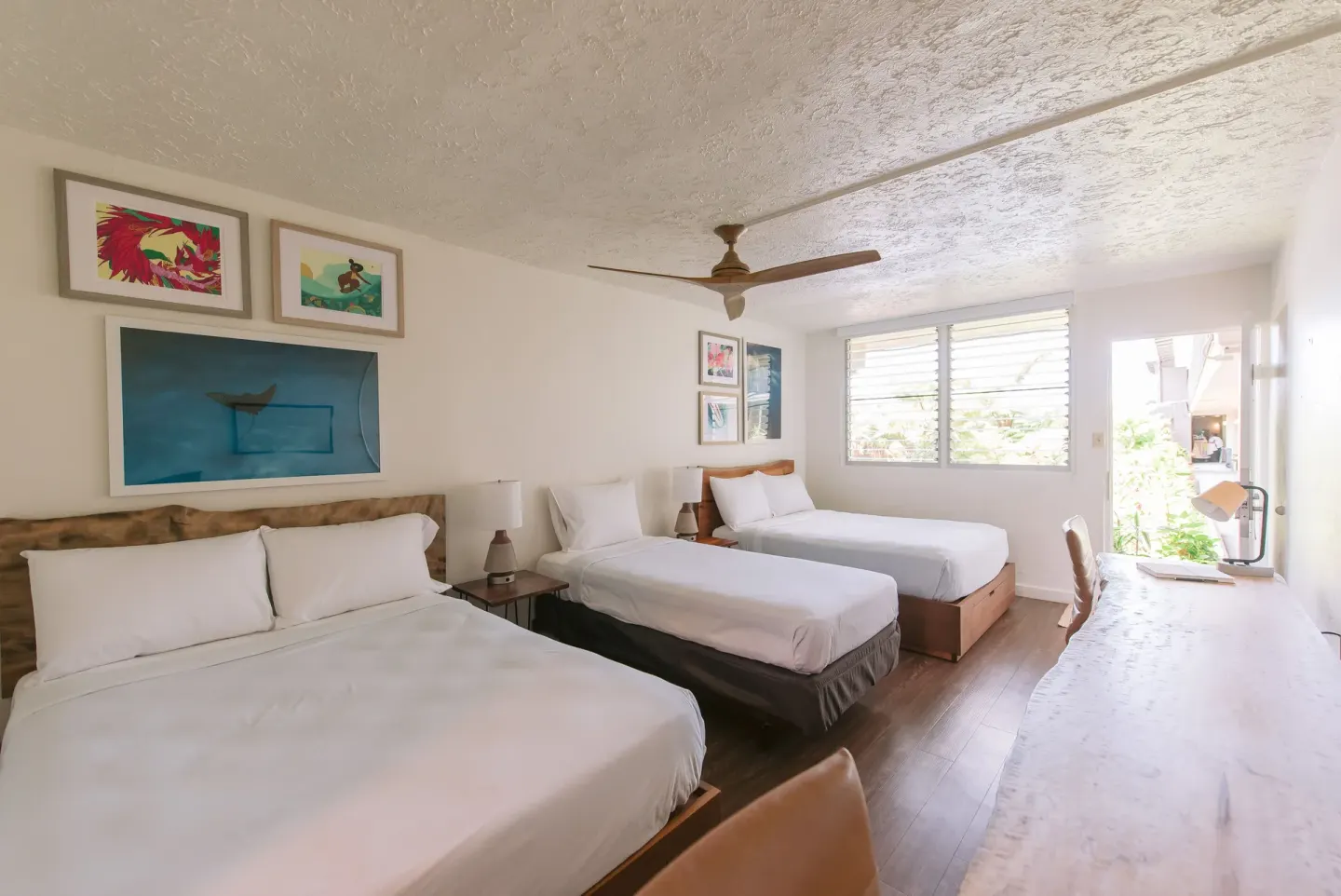 Spacious guest room with three beds, desk, and open doorway at SCP Hilo Hotel.