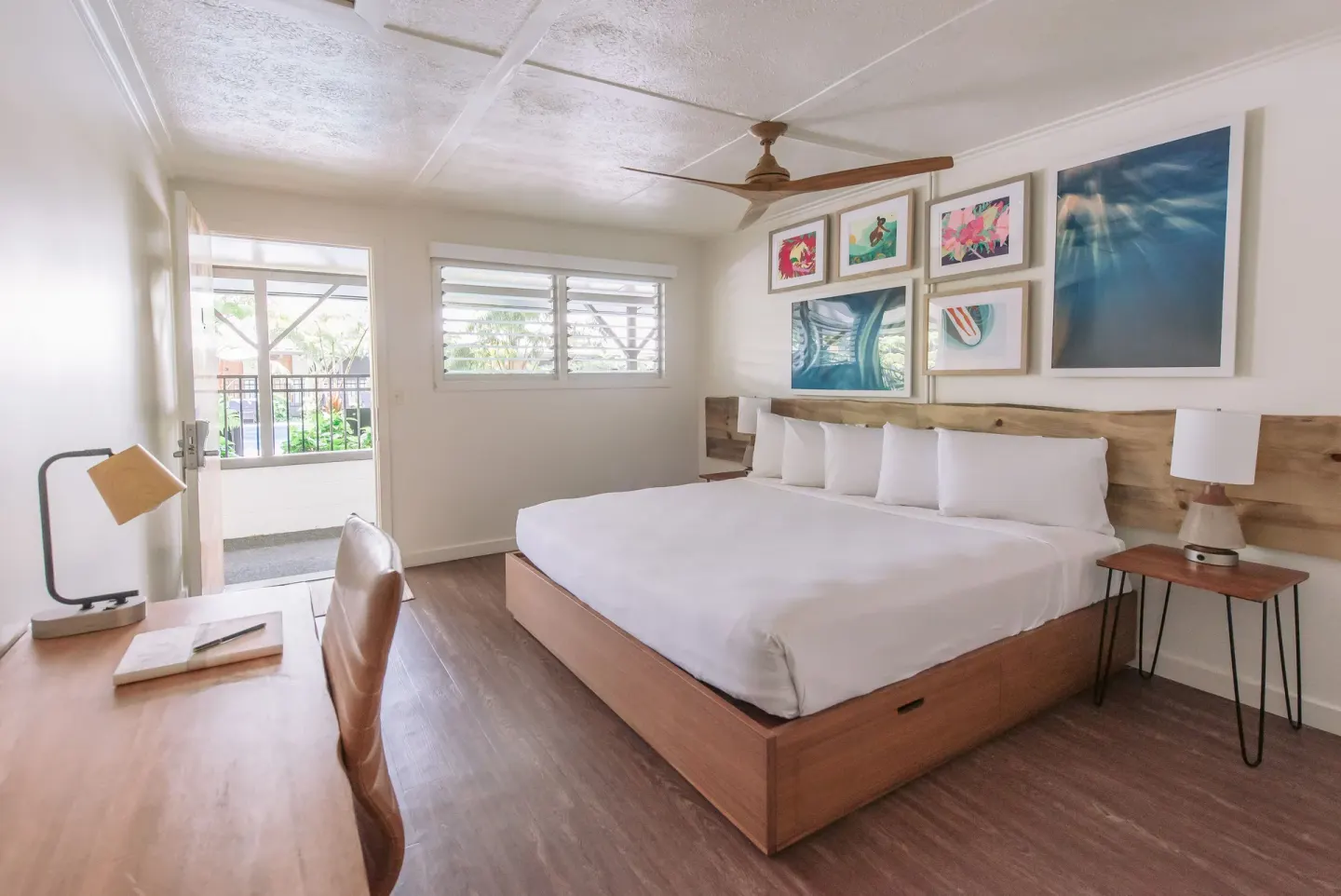 King bed guest room with desk, balcony door, and art wall at SCP Hilo Hotel.