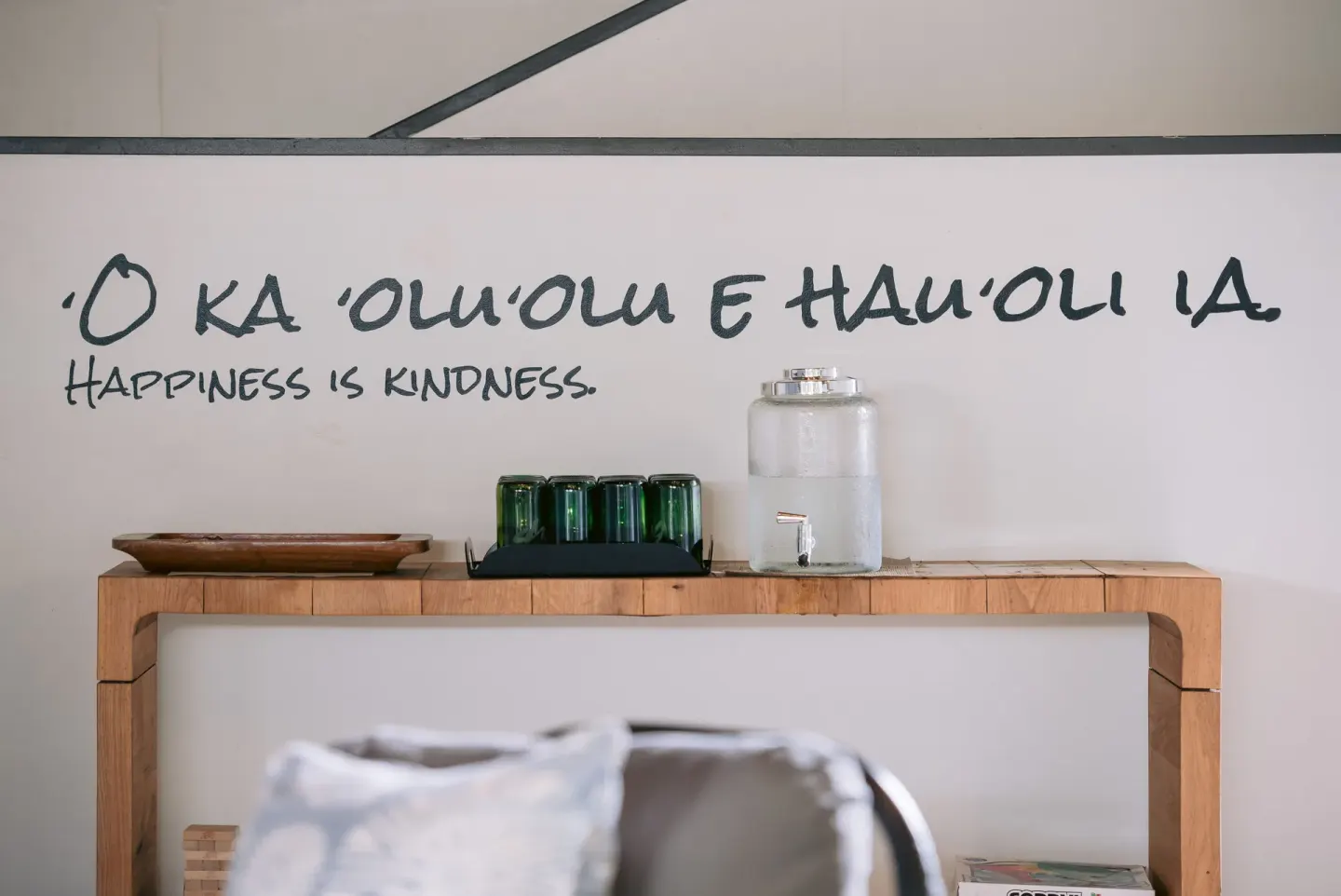 Lobby refreshment station with water, cups, and wall writing at SCP Hilo Hotel.