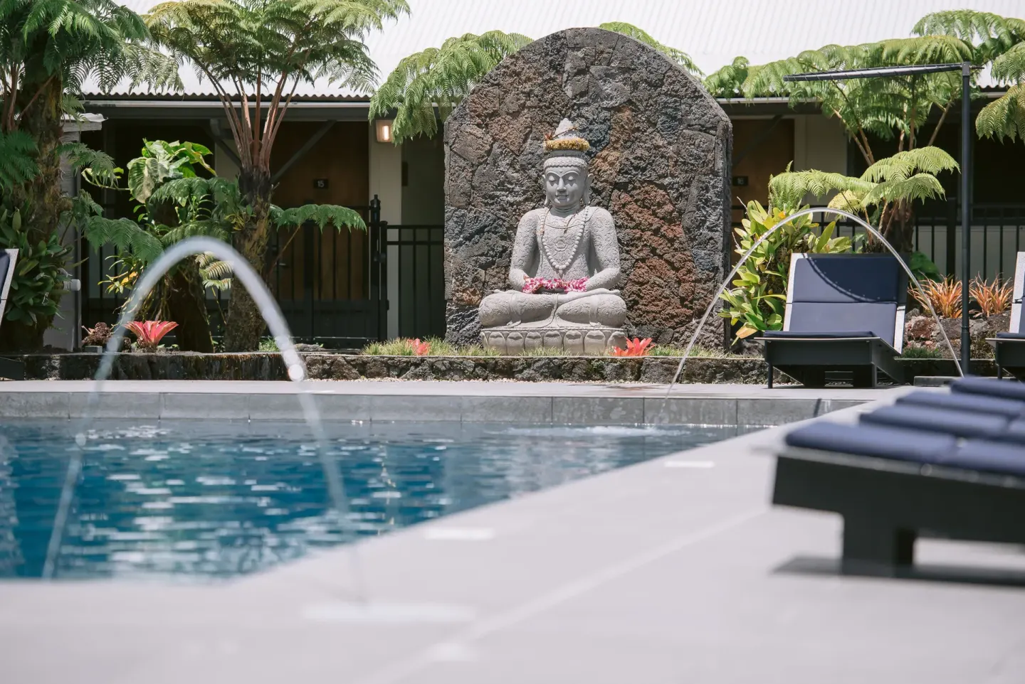 Pool water jets, lounge chairs, and a stone statue at SCP Hilo Hotel.