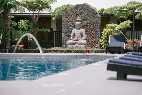 Pool water jets, lounge chairs, and a stone statue at SCP Hilo Hotel.