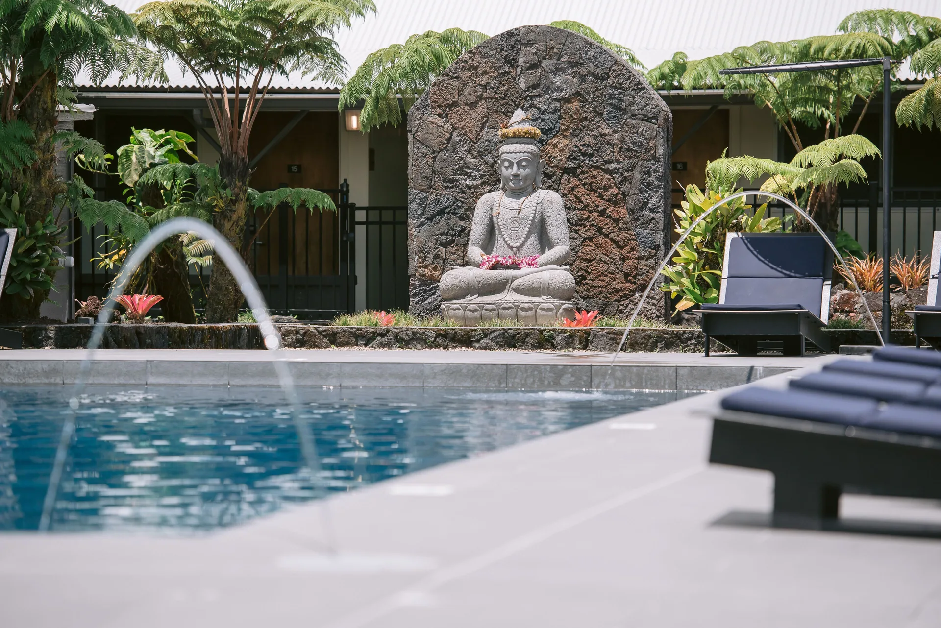Pool water jets, lounge chairs, and a stone statue at SCP Hilo Hotel.