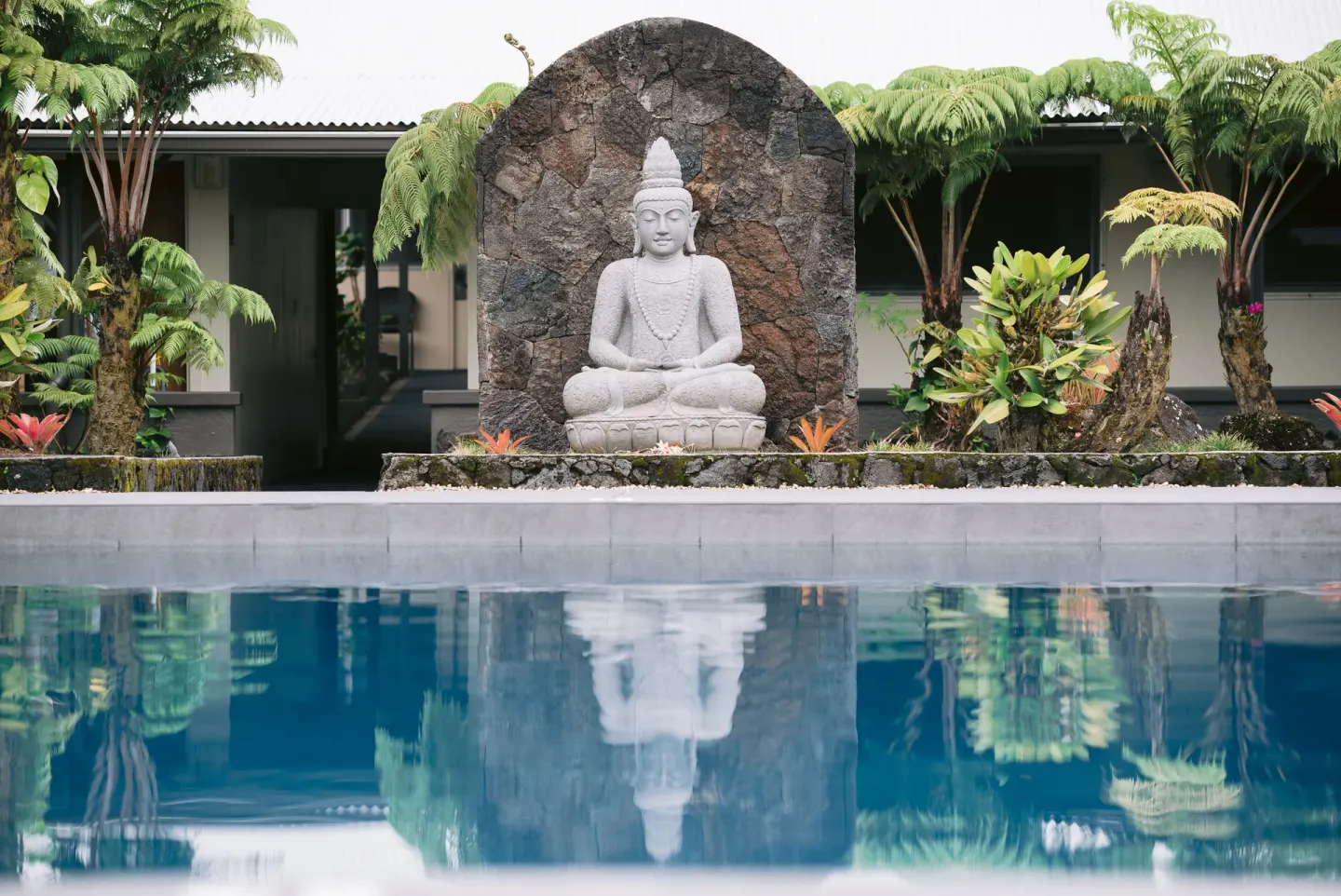 Pool reflection of a seated statue in tropical landscaping at SCP Hilo Hotel.
