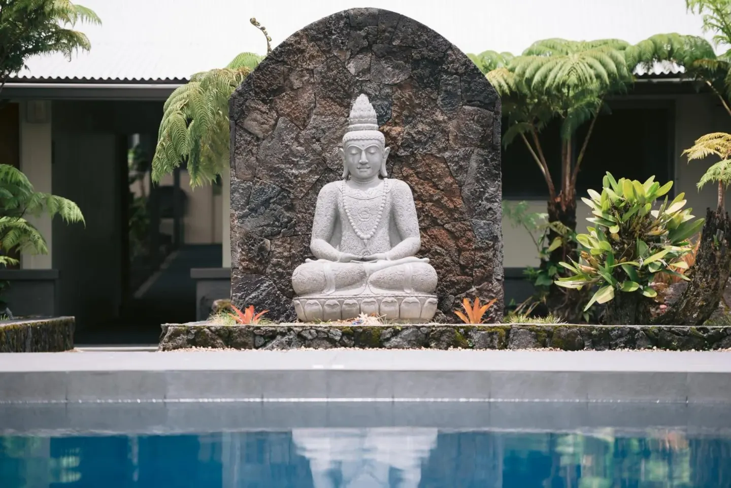 Poolside statue with tropical plants reflected in the water at SCP Hilo Hotel.