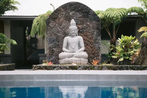 Poolside statue with tropical plants reflected in the water at SCP Hilo Hotel.