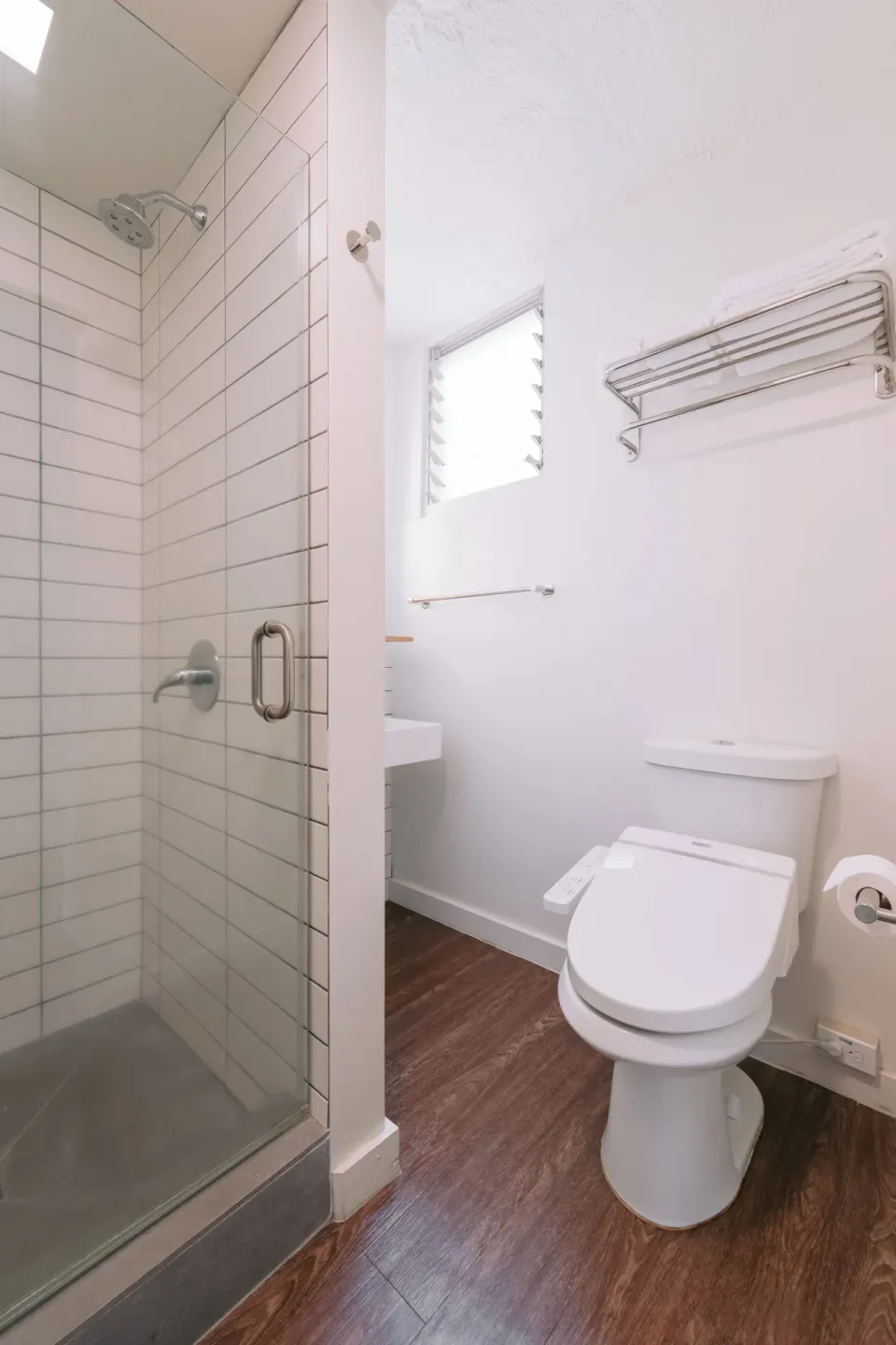 Peaceful Room bathroom with glass shower, toilet, and towel shelf at SCP Hilo Hotel.