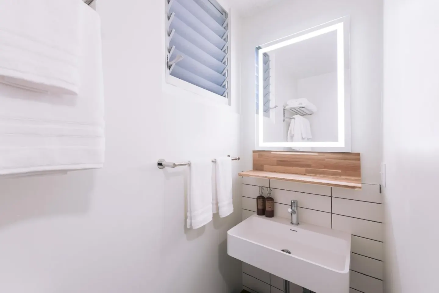 Peaceful Room bathroom sink with lit mirror and towels at SCP Hilo Hotel.
