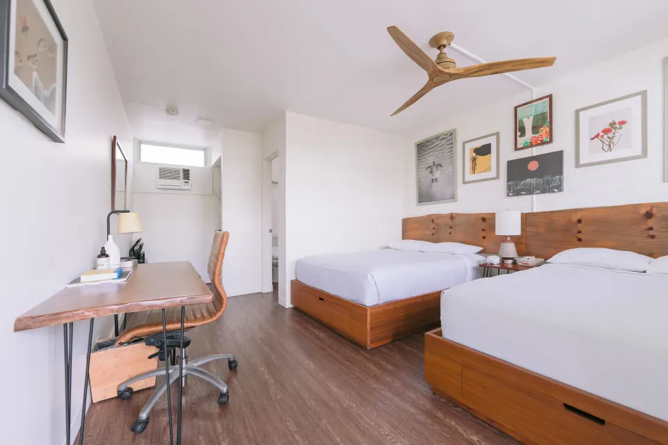 Peaceful Room with two beds, desk, chair, and ceiling fan at SCP Hilo Hotel.