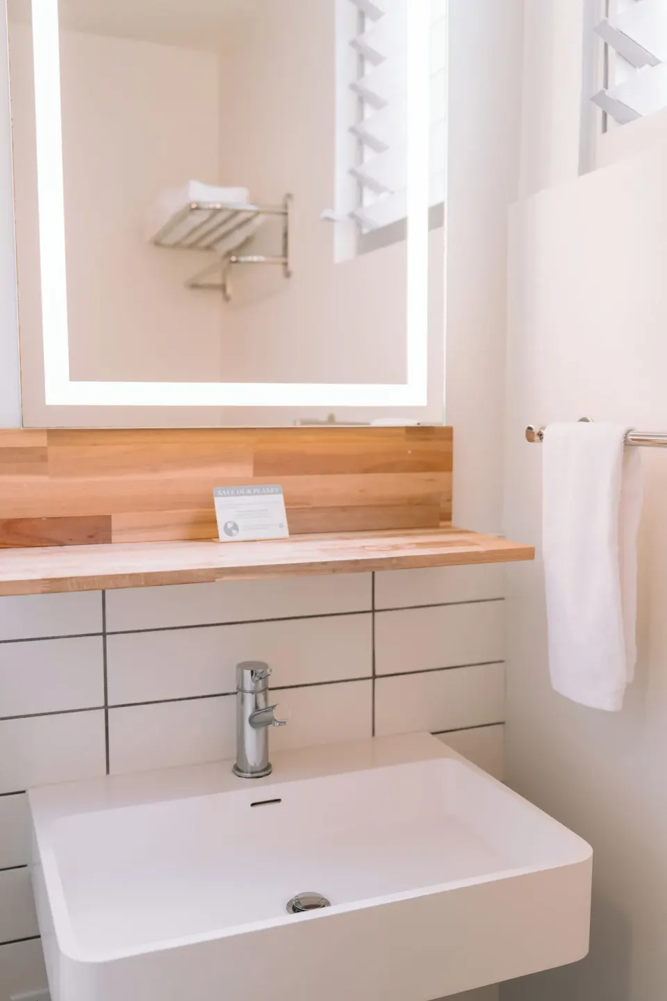 Peaceful Room vanity with lit mirror, sink, towel, and louvered window at SCP Hilo Hotel.