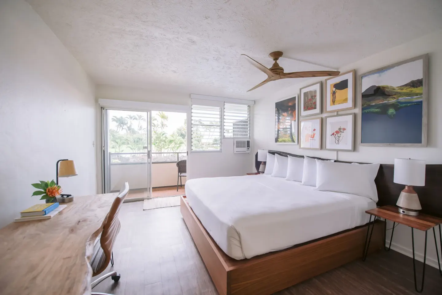 Bay View guest room with king bed, desk, balcony, and palm trees at SCP Hilo Hotel.
