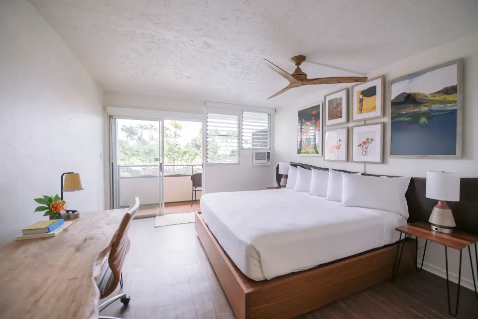 Bay View guest room with king bed, desk, balcony, and palm trees at SCP Hilo Hotel.