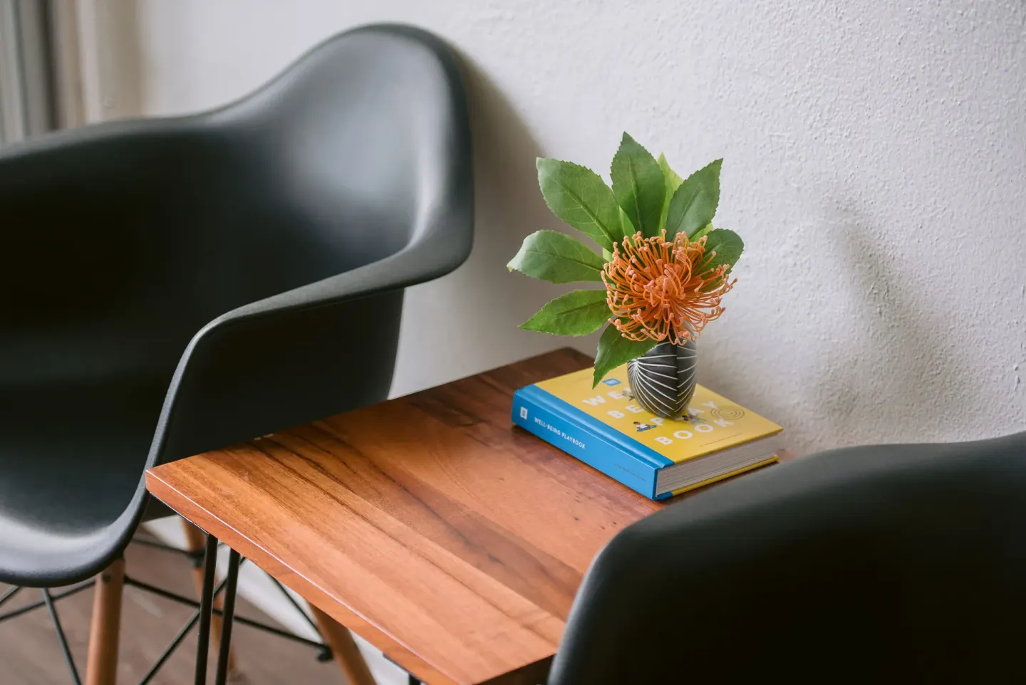 Guest room sitting area with black chairs, wood table, flower, and book at SCP Hilo Hotel.