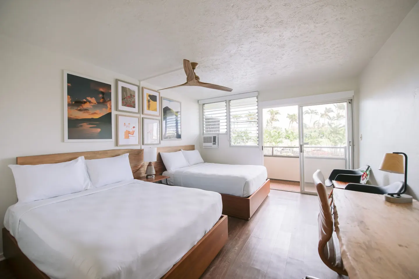 Bay View guest room with two beds, desk, seating, and balcony doors at SCP Hilo Hotel.