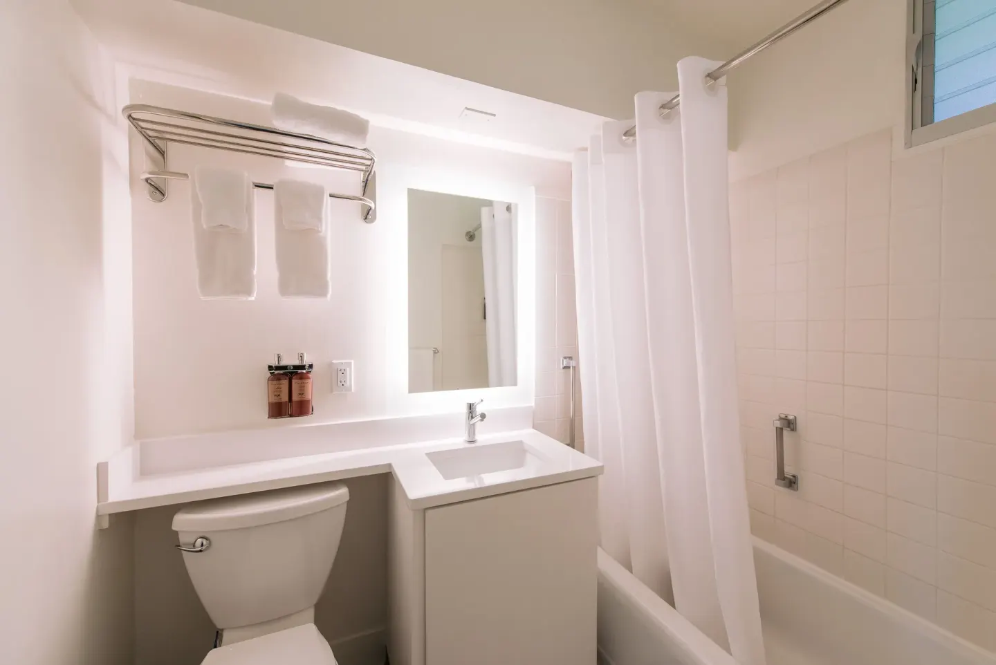Bright guest room bathroom with tub, shower curtain, vanity, and towels at SCP Hilo Hotel.