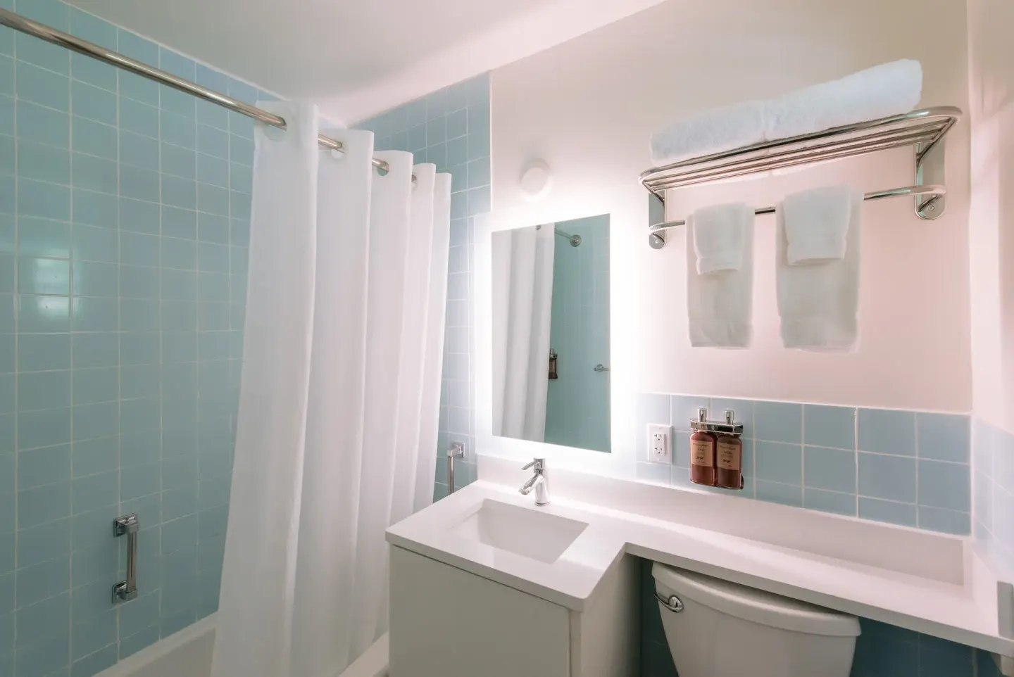 Guest bathroom with blue tile, vanity, towels, and shower curtain at SCP Hilo Hotel.