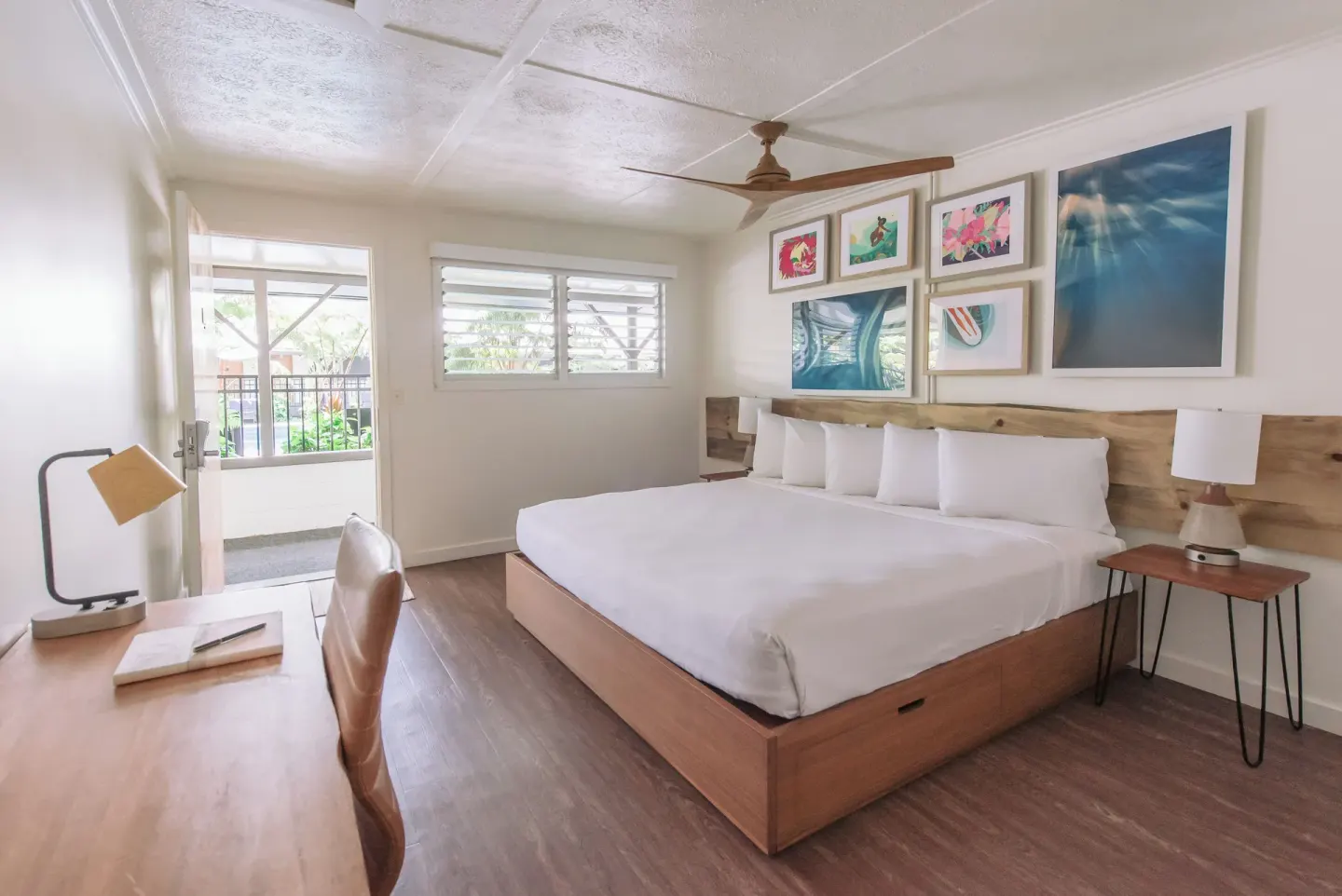 Poolside guest room with king bed, desk, wall art, and open door at SCP Hilo Hotel.