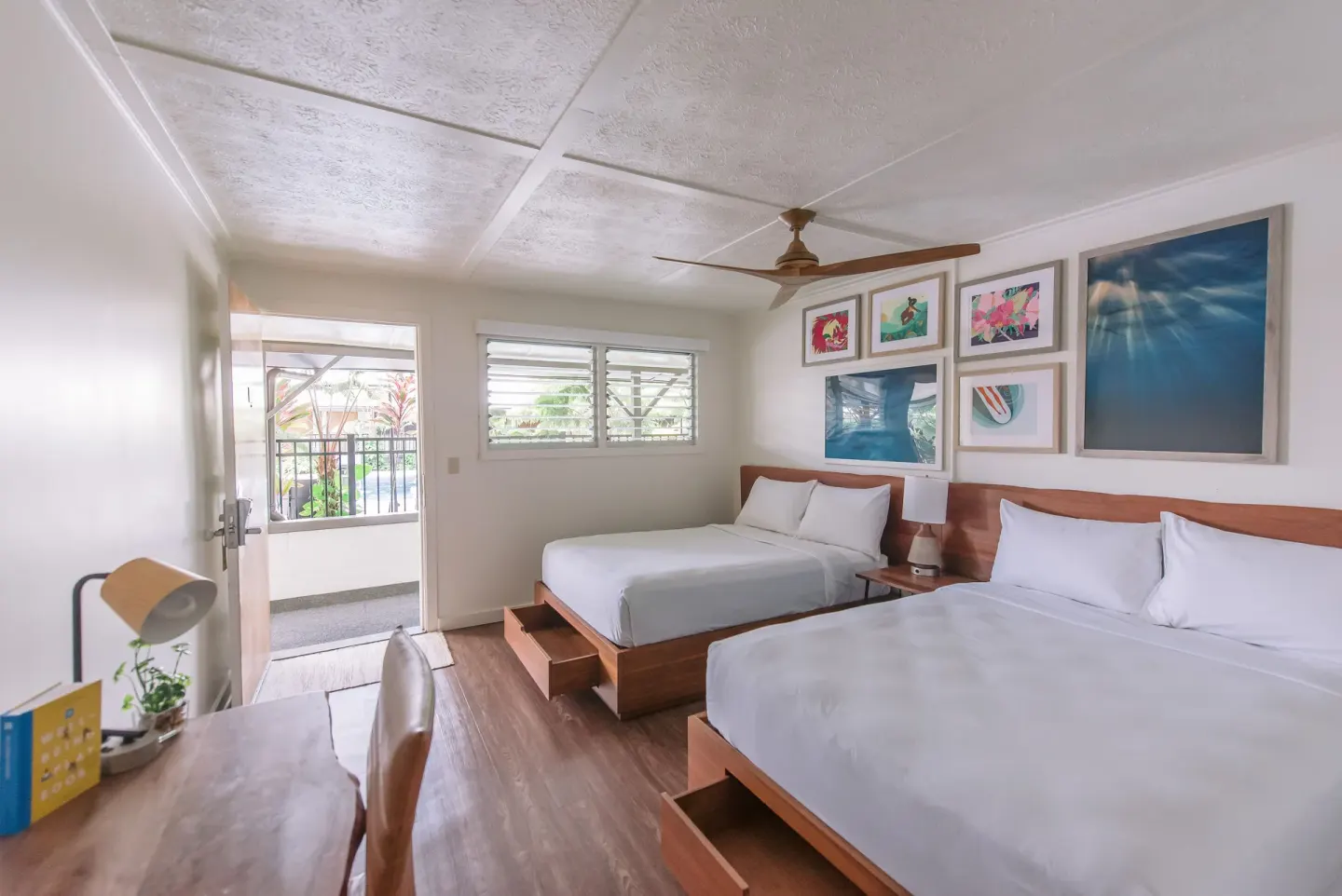 Poolside guest room with two beds, desk, and open balcony door at SCP Hilo Hotel.