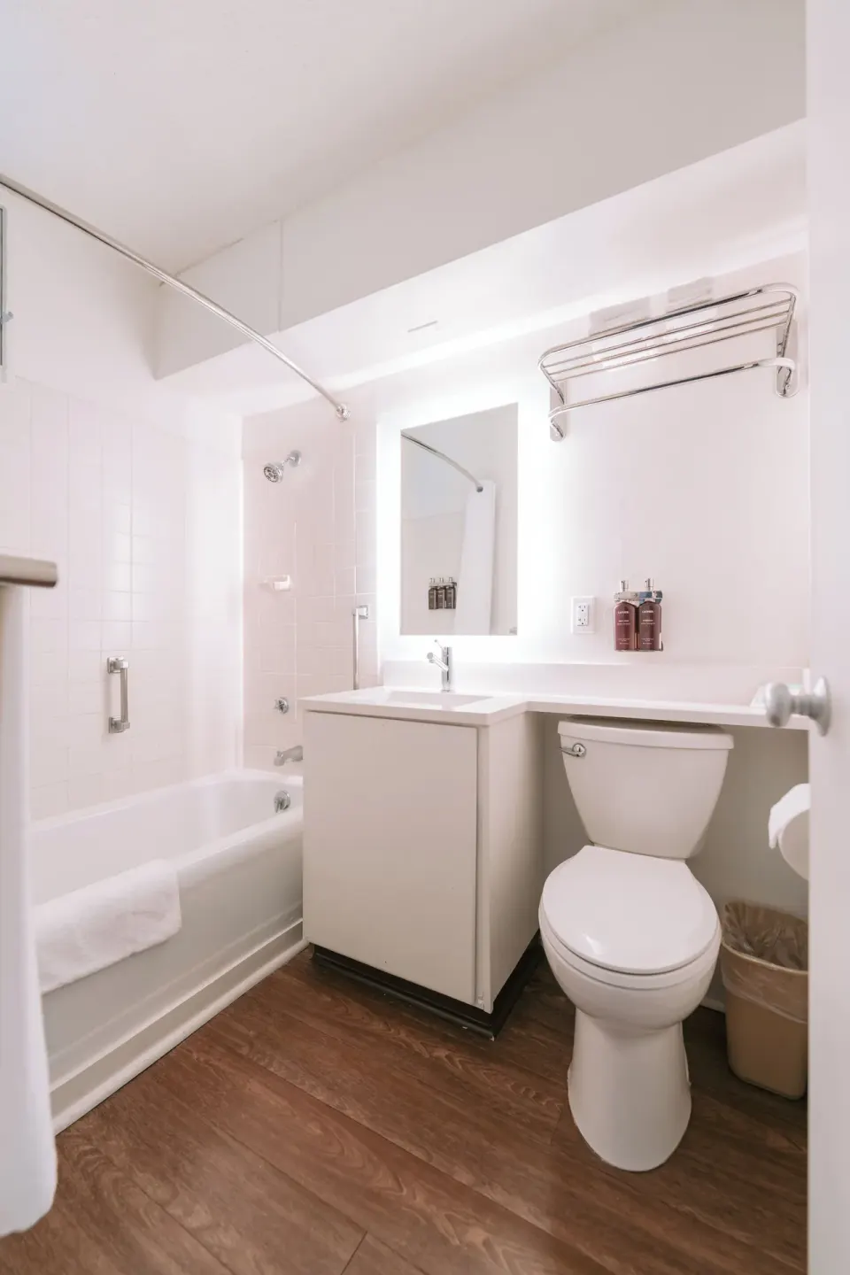 Guest room bathroom with open door, tub, toilet, vanity, and towels at SCP Hilo Hotel.