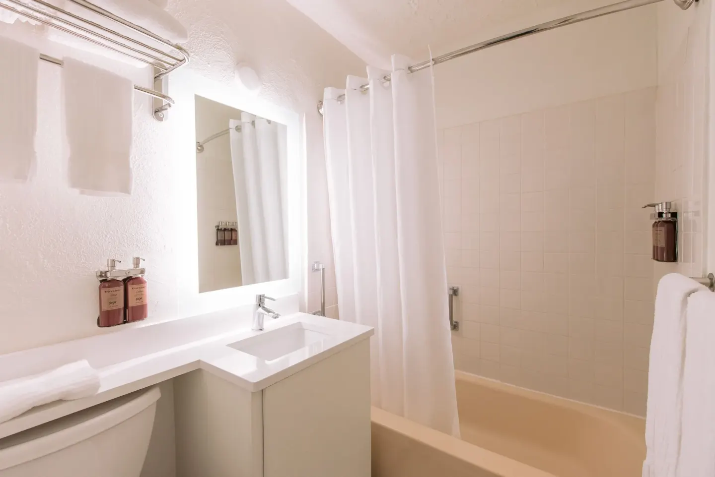Guest room bathroom with vanity, mirror, towels, and shower curtain at SCP Hilo Hotel.