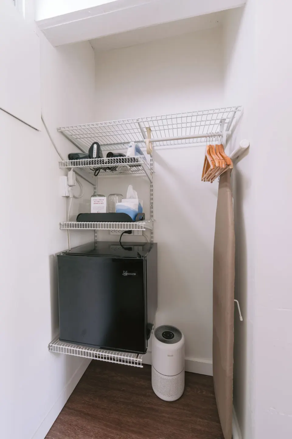 Guest room closet with mini fridge, shelves, hangers, and ironing board at SCP Hilo Hotel.