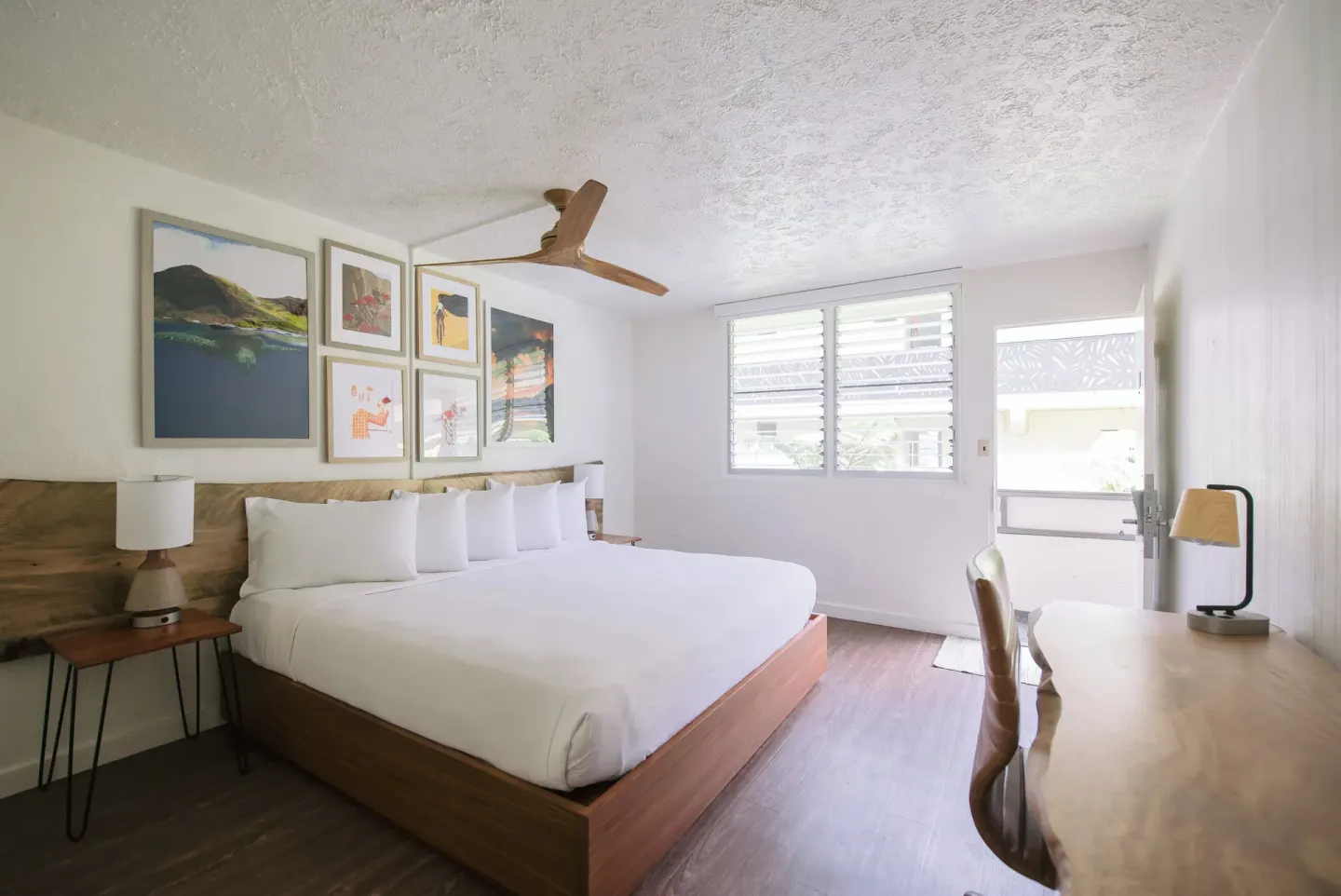 Guest room with king bed, desk, artwork, and open doorway at SCP Hilo Hotel.