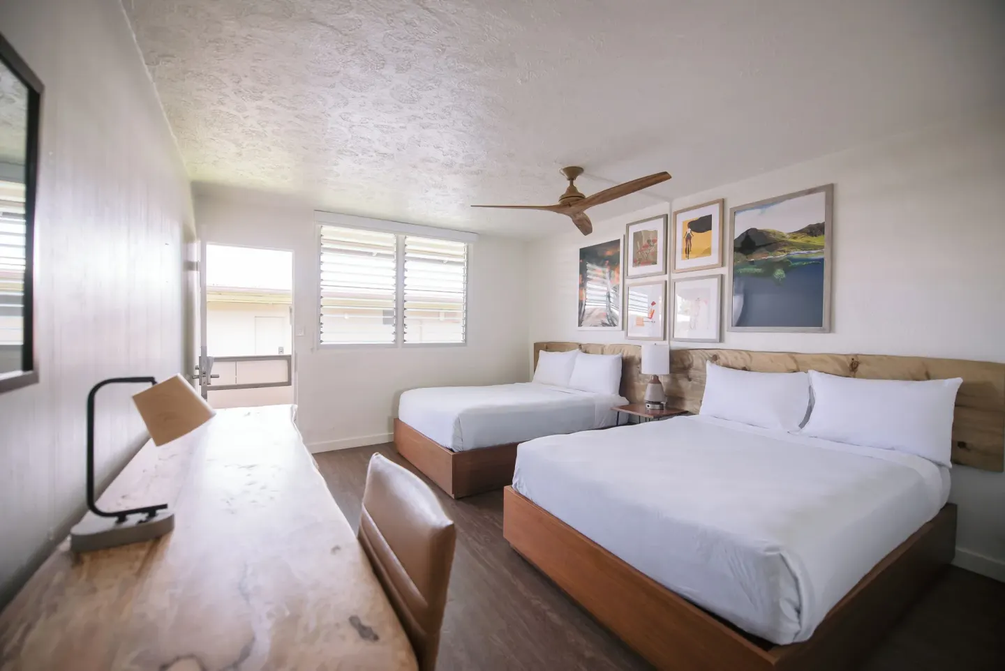 Two-bed guest room with desk lamp, ceiling fan, and framed art at SCP Hilo Hotel.