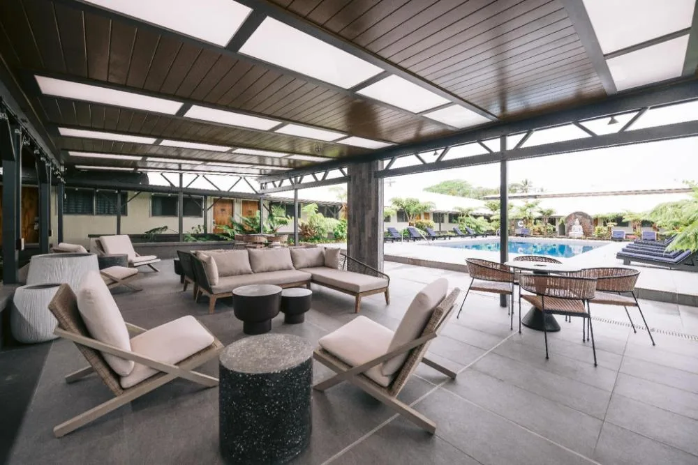 Covered poolside lounge at SCP Hilo Hotel with cushioned seating and tables near the pool.