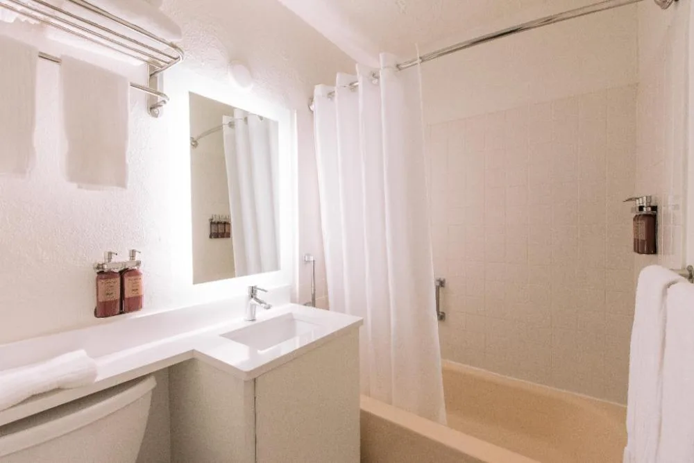 Standard room bathroom with vanity, mirror, tub, and white shower curtain at SCP Hilo Hotel.