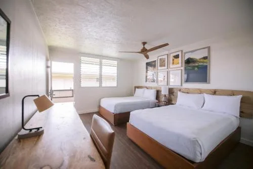 Standard room with two beds, desk, wall art, and window at SCP Hilo Hotel.