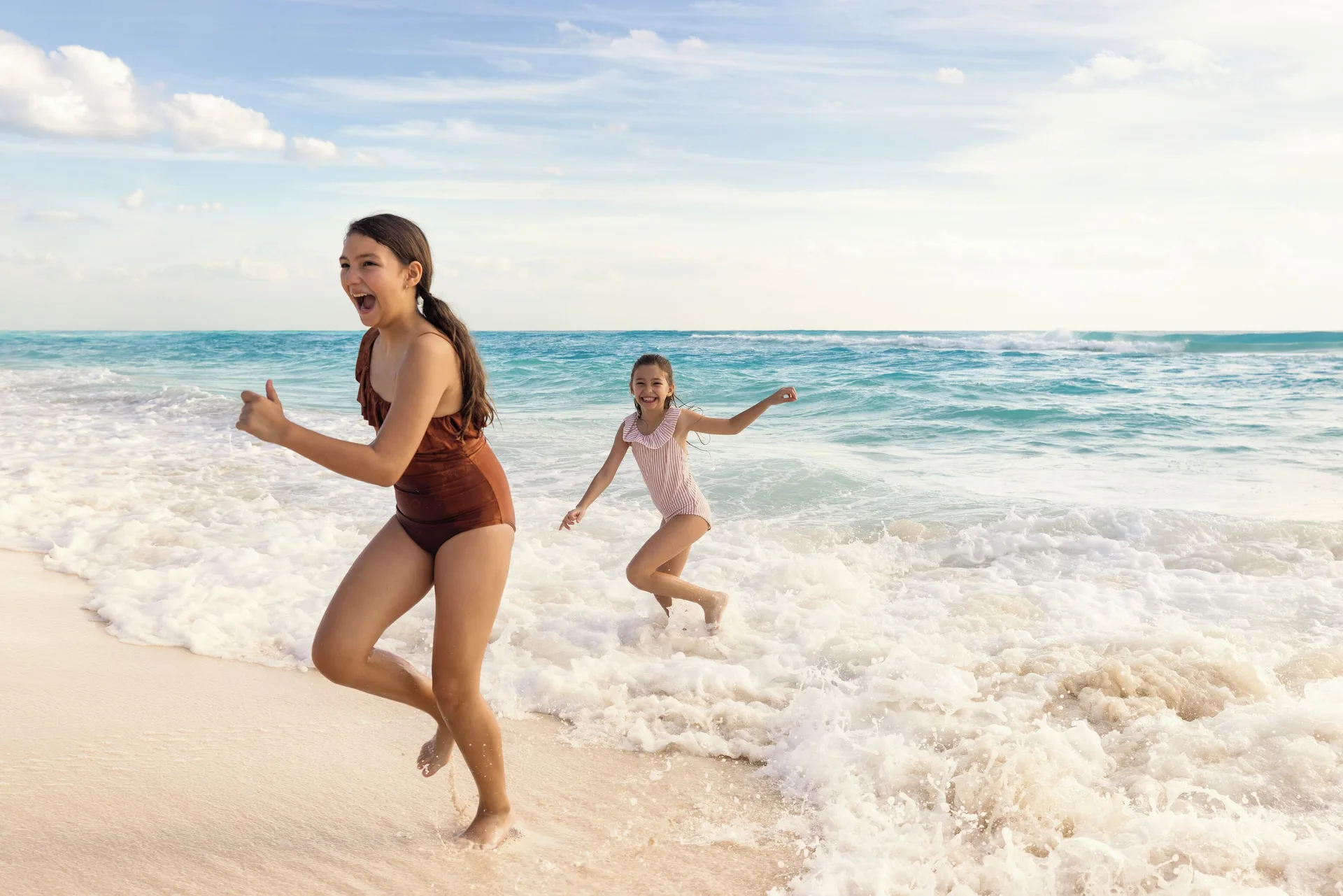 Two children run through ocean surf on the beach at Seadust Cancún Family Resort.
