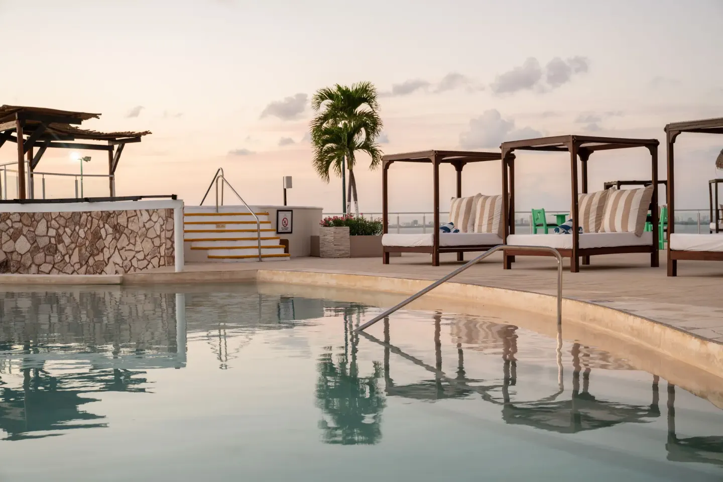 Calm pool with canopy daybeds at dusk at Seadust Cancún Family Resort.