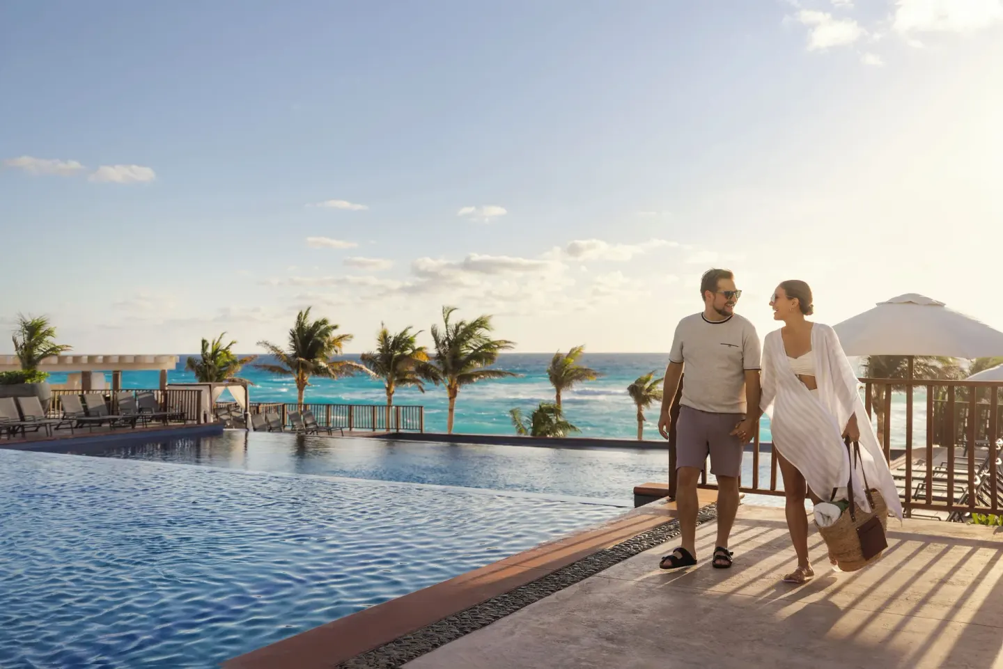 Couple walks beside an ocean-view pool at Seadust Cancún Family Resort.